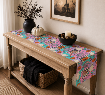 A colorful Halloween-themed table runner with cartoon ghosts, pumpkins, and spooky patterns draped over a wooden console table in a styled home interior.