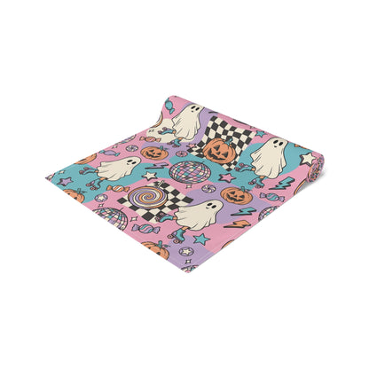 Rolled up Table runner featuring a colorful Halloween pattern with ghosts, pumpkins, stars, candy, and checkered squares on a pink, purple, and teal background. cotton twill fabric