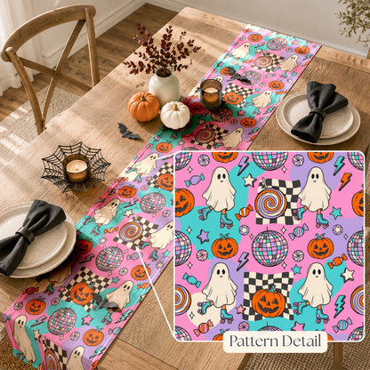 A Halloween-themed table runner displayed on a wooden dining table, with a matching inset detail box showing the pattern. The runner features a colorful print of ghosts, pumpkins, candy, stars, and disco balls on pink, purple, and teal backgrounds.